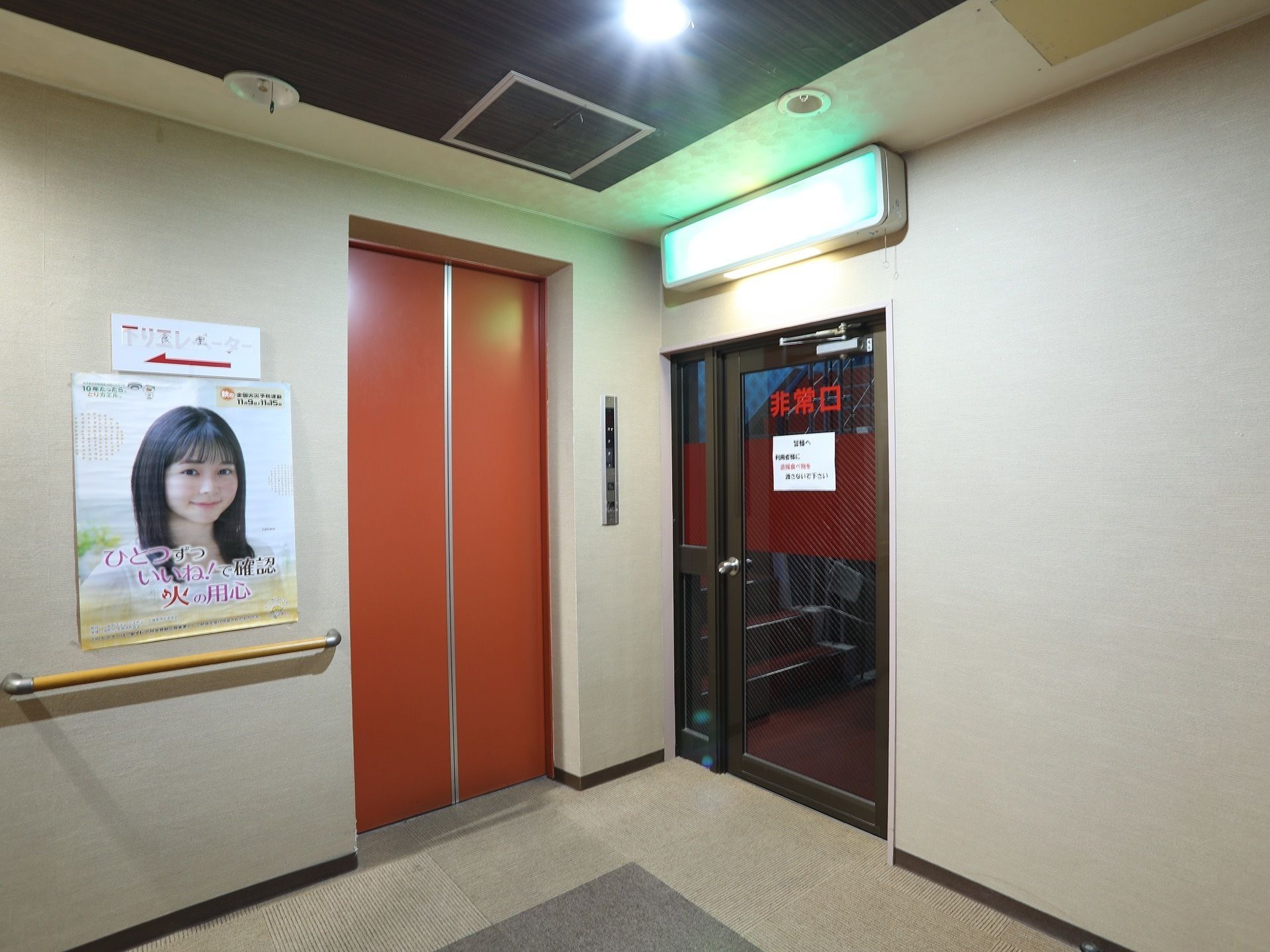 広々としたエレベーターホール横には非常口へつながるドアがあり、頭上には大きな非常灯が設置されている。壁には手すりがある。