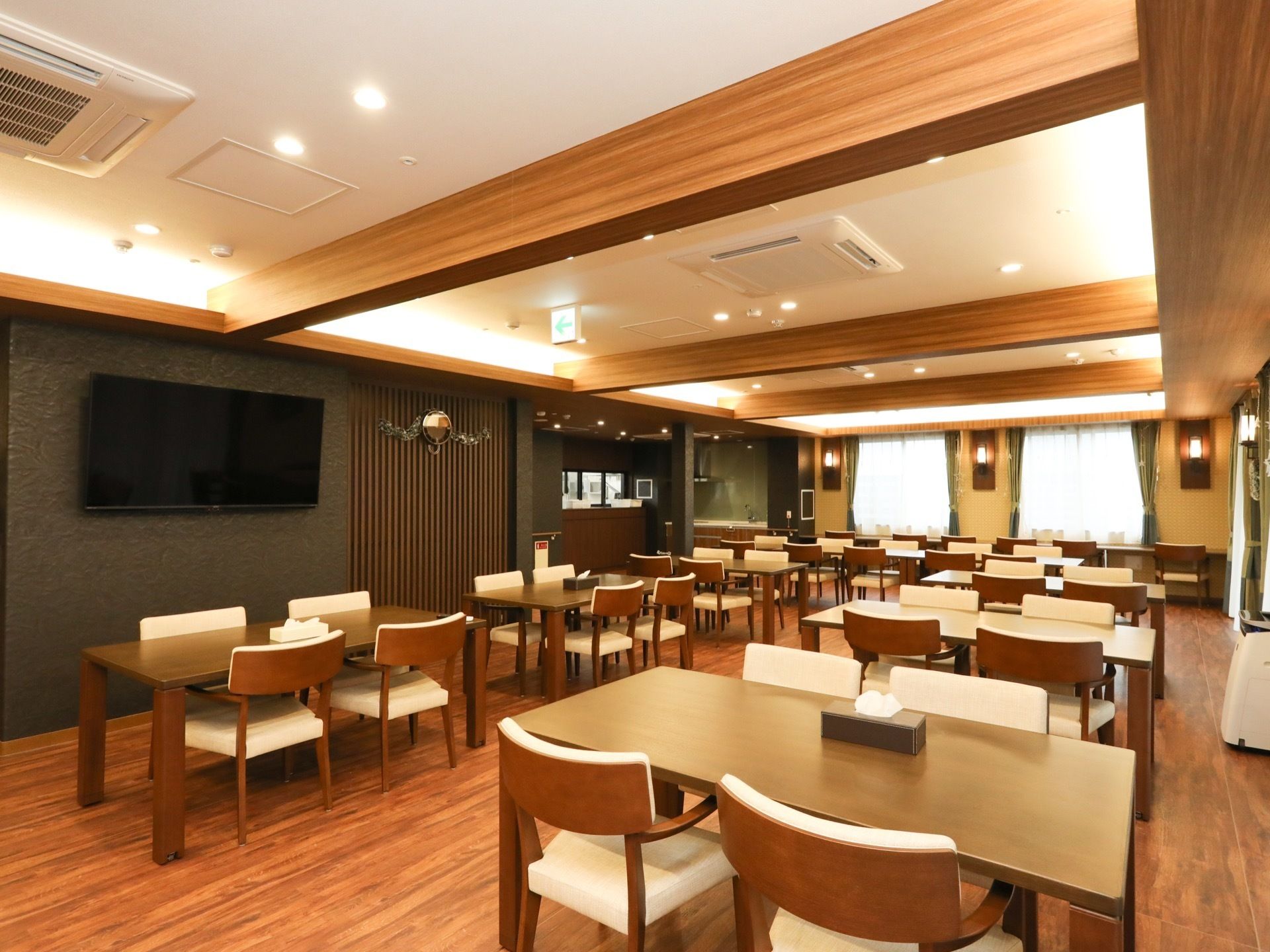 天井に存在感ある柱が設けられた広い食堂である。複数のテーブルと椅子が配置されている。壁にはテレビがある。