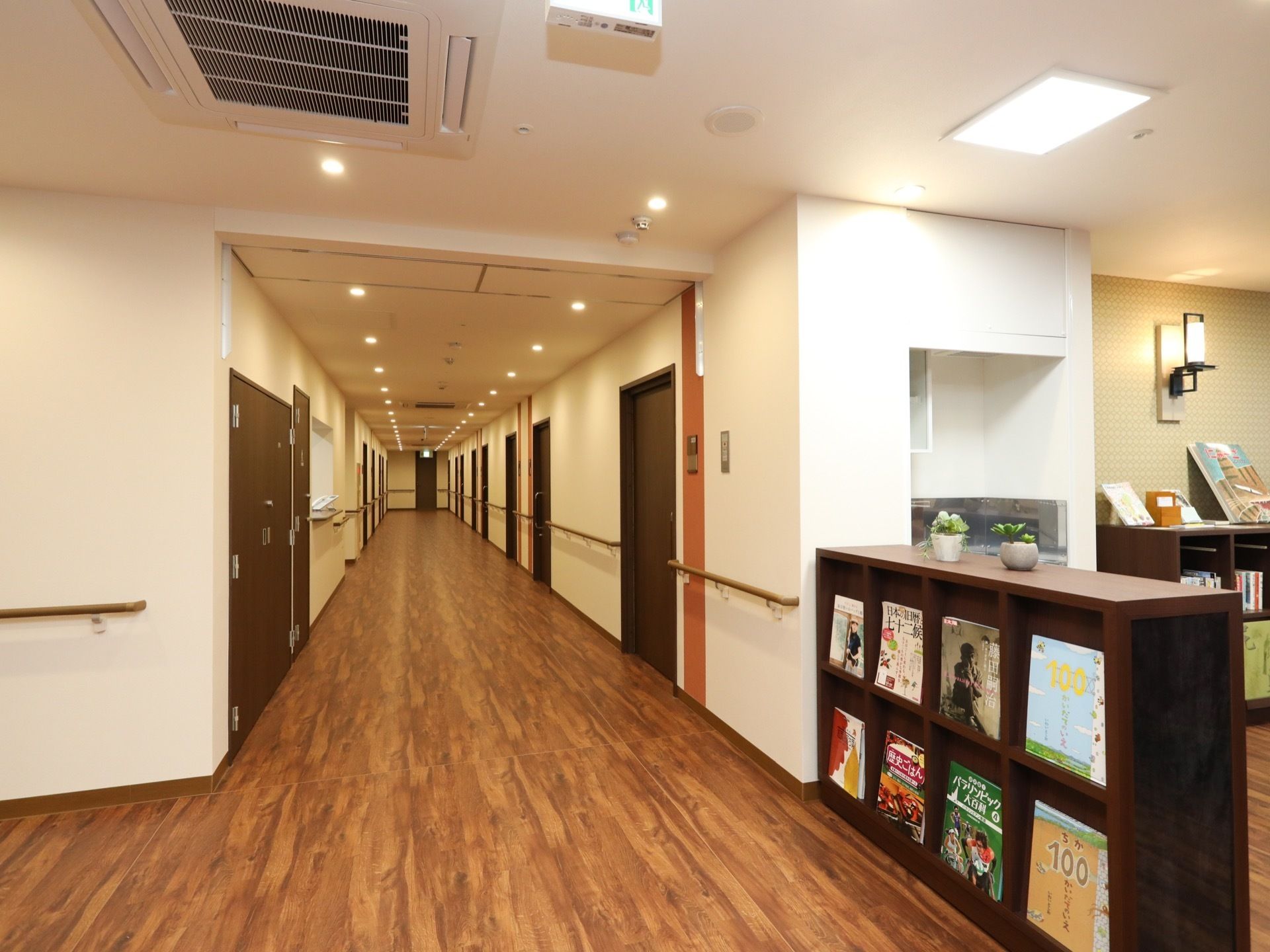 茶色の木目調タイプの通路である。床面はフラットで、バリアフリー化されている。天井には照明が２列配置されている。