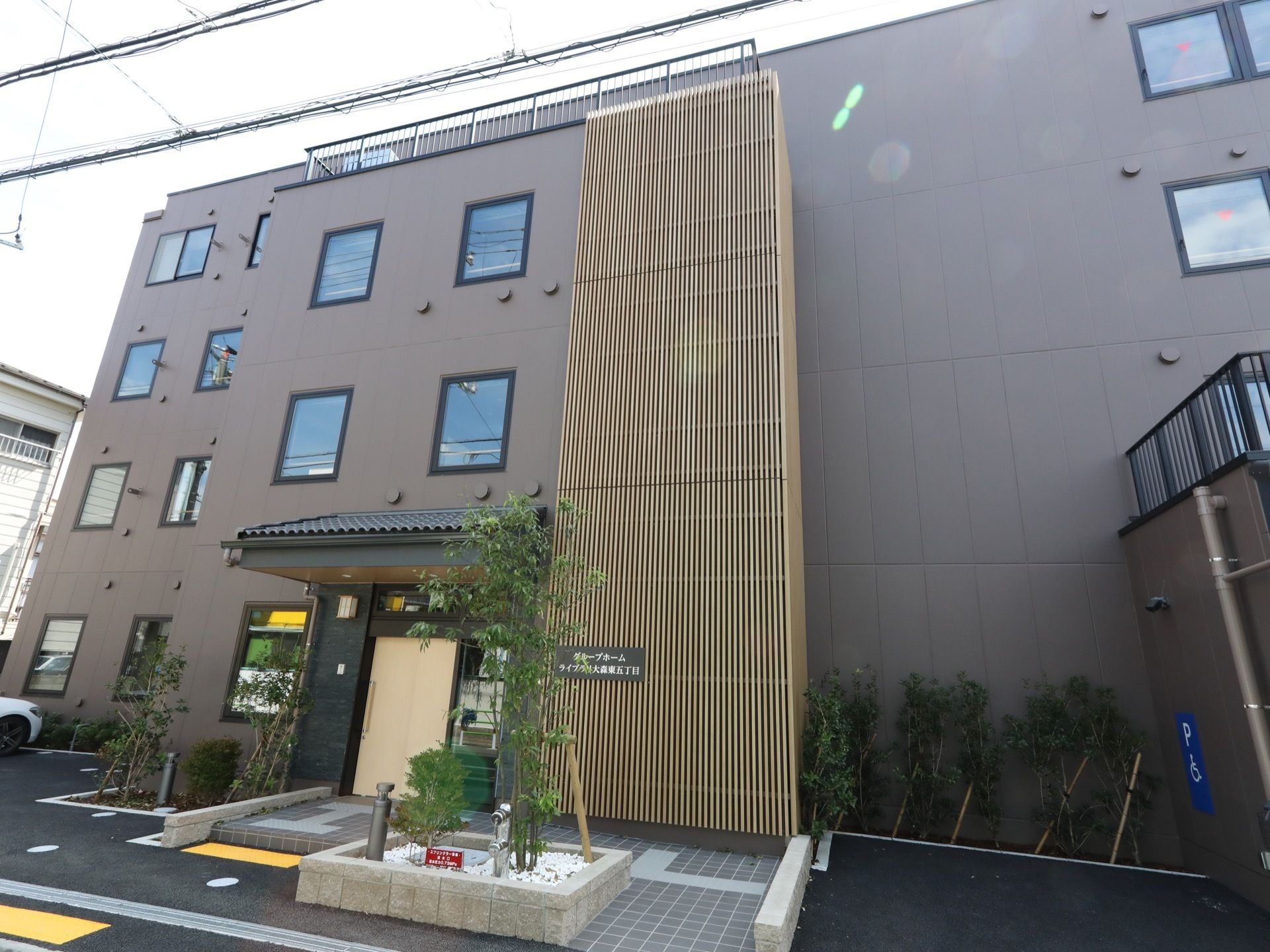 ブラウン系の外壁に和のテイストを盛り込み、設計された施設外観となっている。植栽があり、点字ブロックやスロープが完備されている。