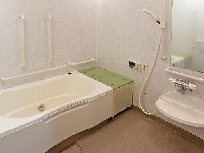 一般の家庭と同じようなサイズの浴槽が置かれた白い浴室にはシャワーと手すり、ベンチも設置されている。