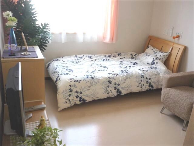 テレビやタンスなどを設置した居室には、花柄の寝具がセットされたベッドがあり、そのそばには緊急通報装置がある。