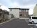 広い駐車場があり、たくさんの窓が付いた建物。ブラウンとベージュの２階建ての建物は明るい雰囲気。