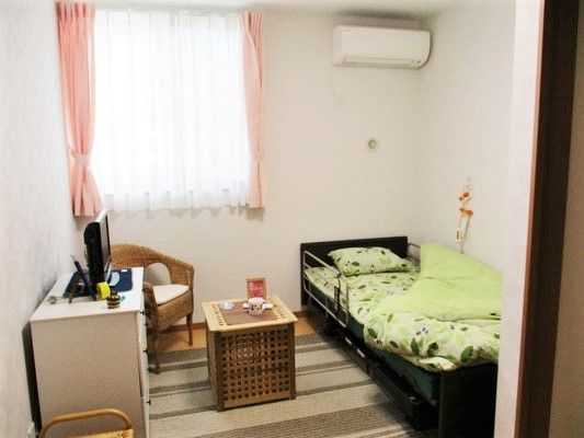 寝具がセットされたベッドが置かれた部屋には、テレビやいす、タンスもある。