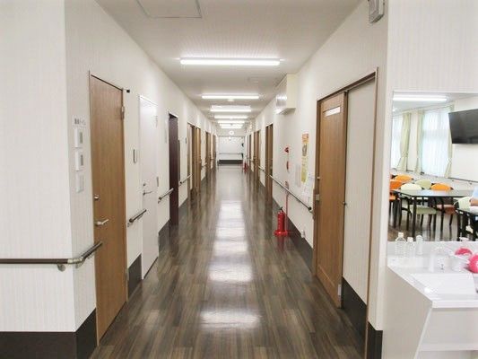 まっすぐな廊下には両側に手すりが付き、ダークブラウンの居室ドアが並び、消火器も置かれている。