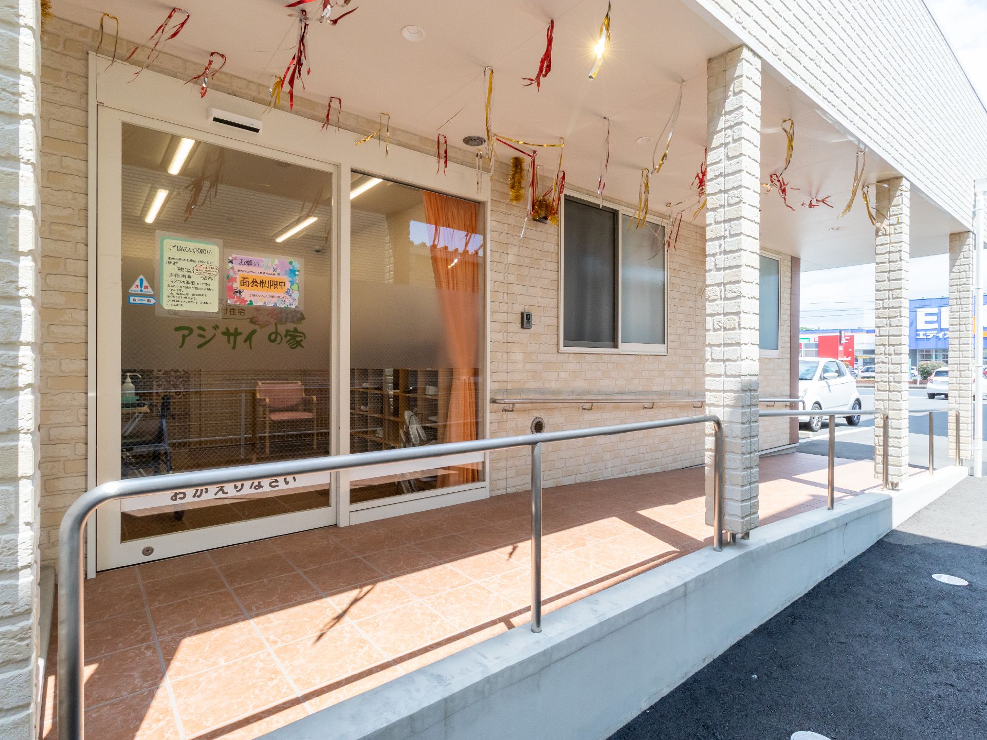 カーディガンを着た高齢女性が車いすに座り、遠くを指さしている。エプロンを付けた若い女性スタッフが一緒に見ている。