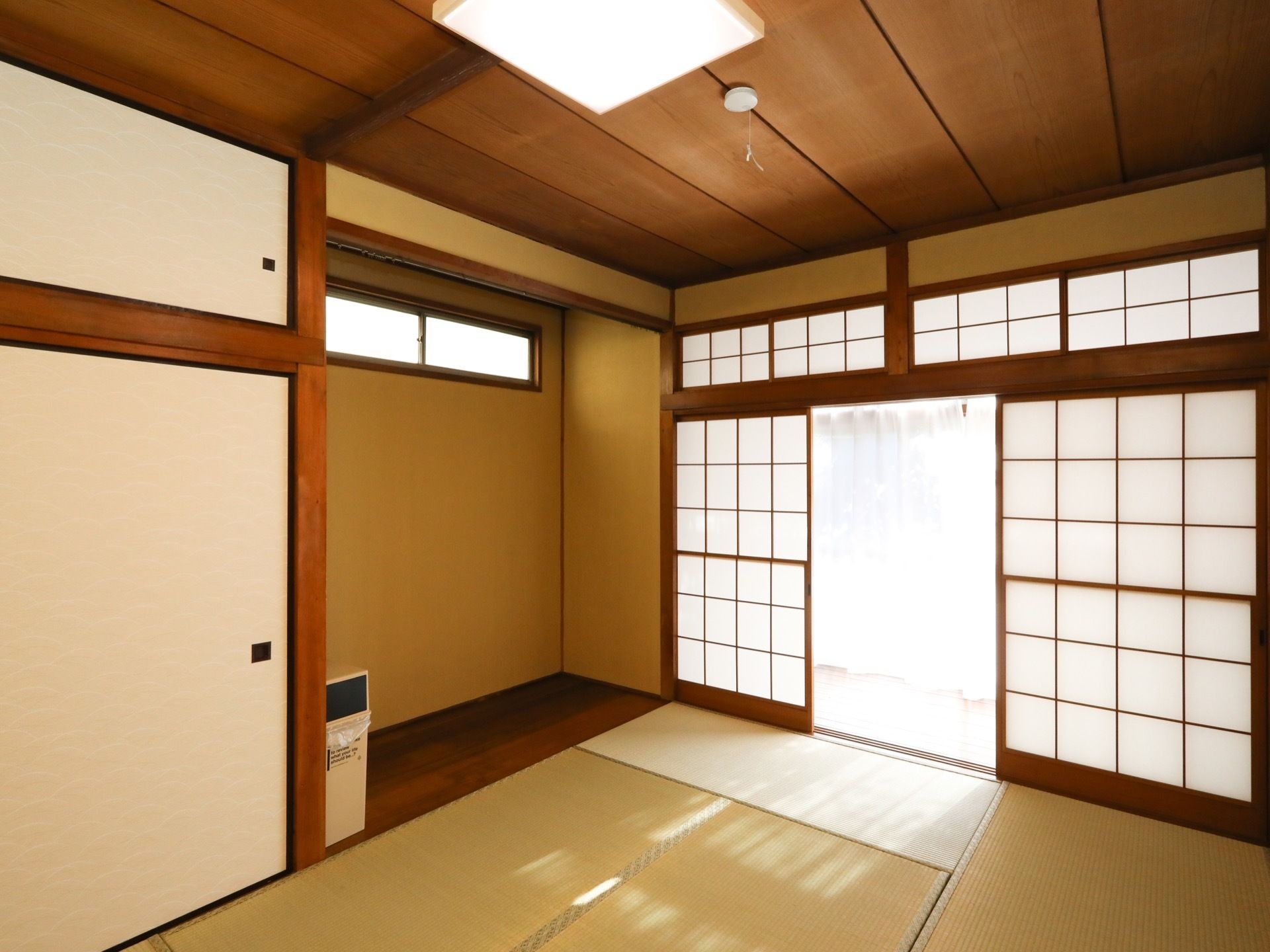 ふすまの押し入れがある、和室の居室である。障子戸の奥には廊下があり、白いレースのカーテンがかかっている。