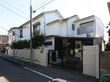 白い壁の2階建て建物である。周囲には白いブロック塀があり、敷地内には、複数の木が植えられている。また、敷地横には電柱がある。