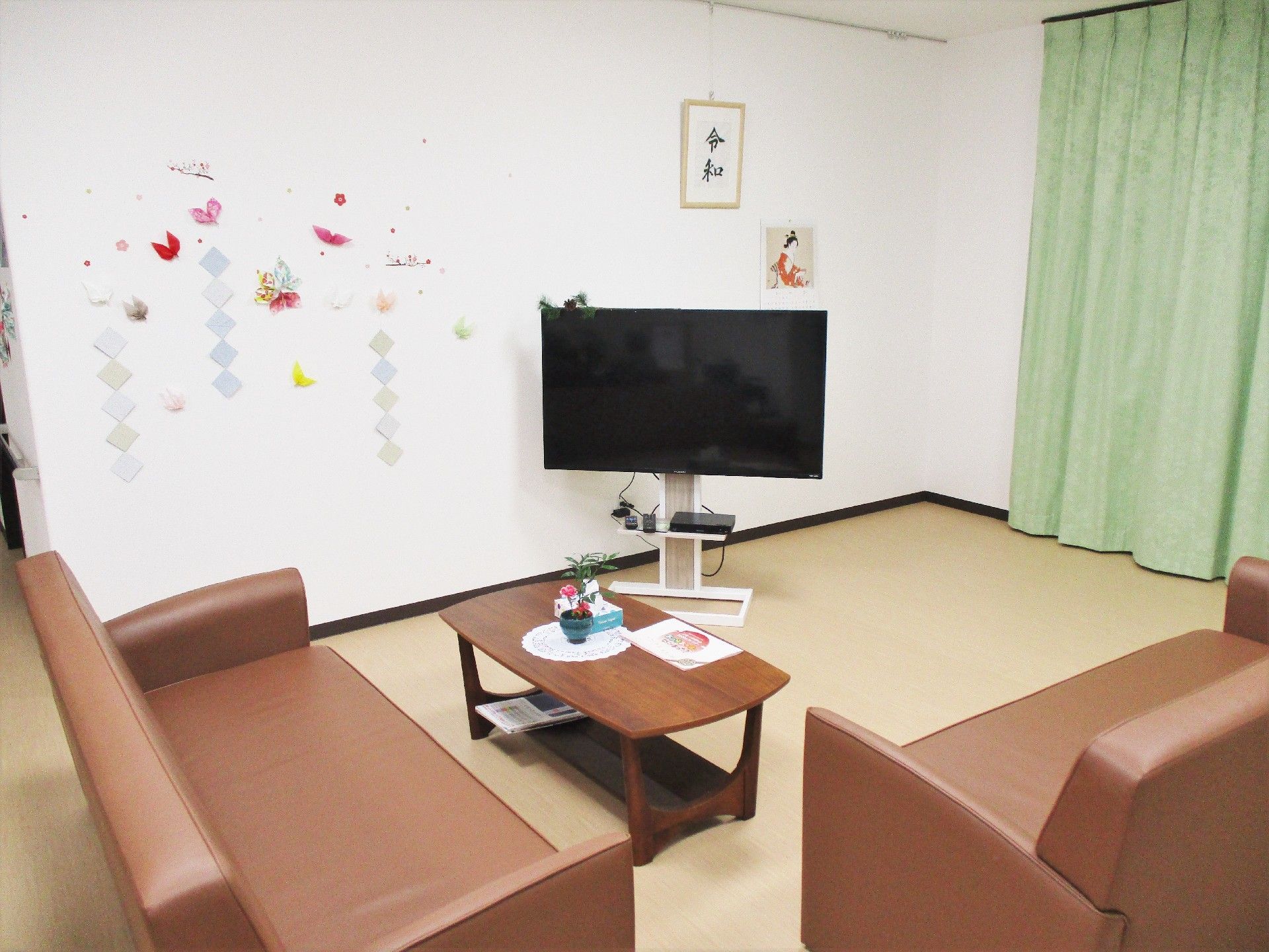 緑のカーテンが付けられた窓があり、ブラウンのソファの応接セットがテレビを見やすい位置に置かれている。