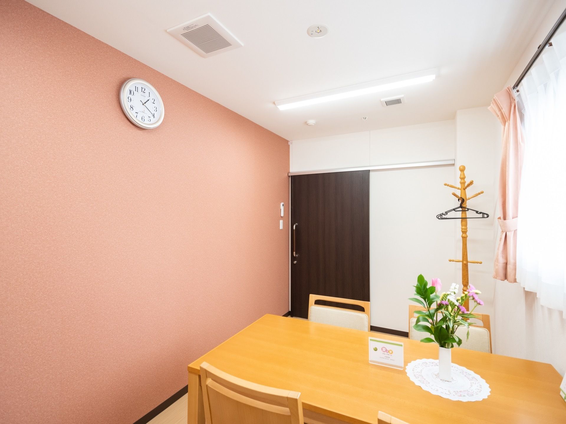 壁とカーテンの色がピンクでコーディネートされた、温かみのある相談室である。テーブルには花が生けられている。