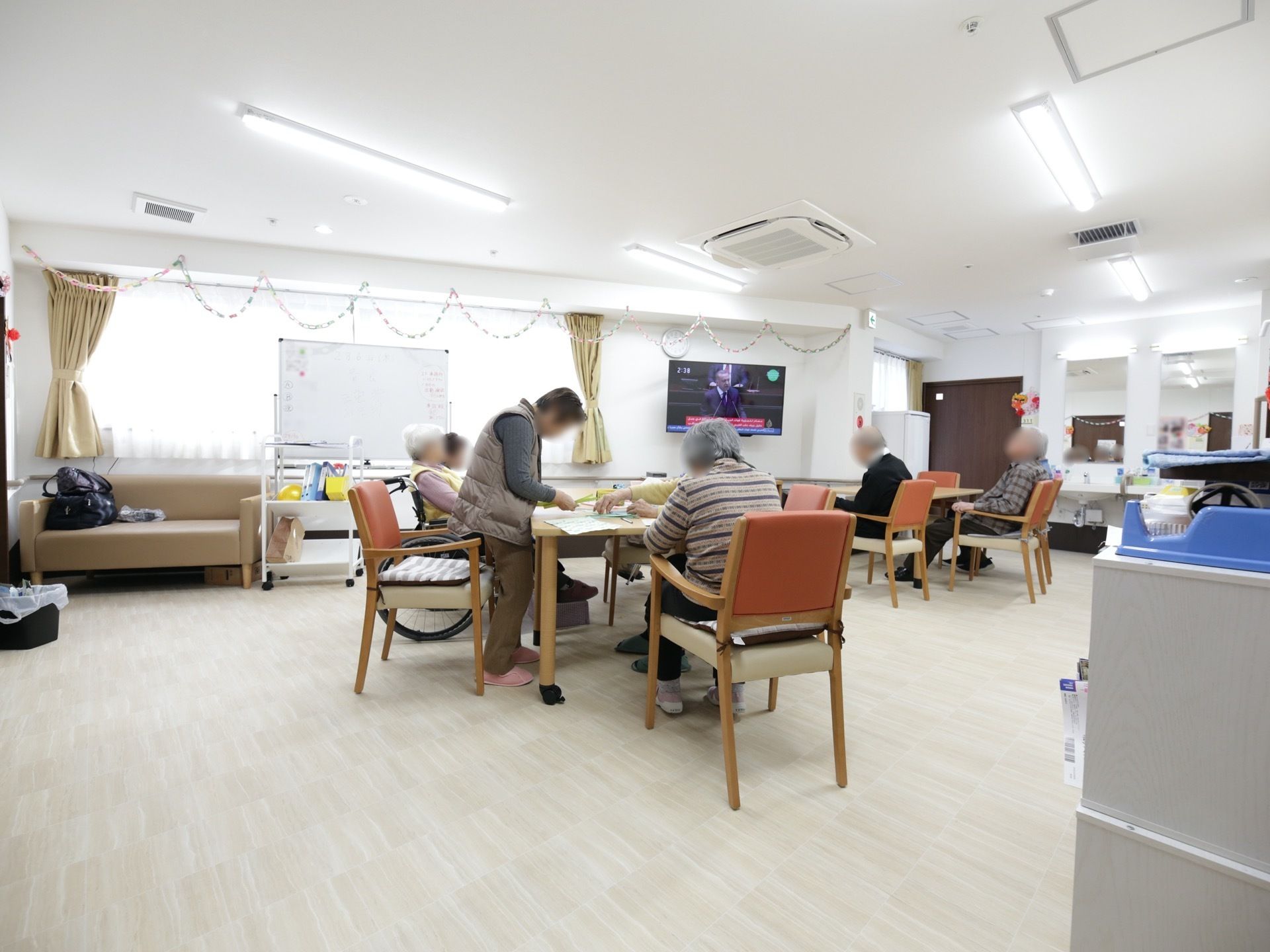 食堂に、横幅のある大きな窓がある。窓際にホワイトボードがあり、その左側にベージュ色のソファが置かれている。
