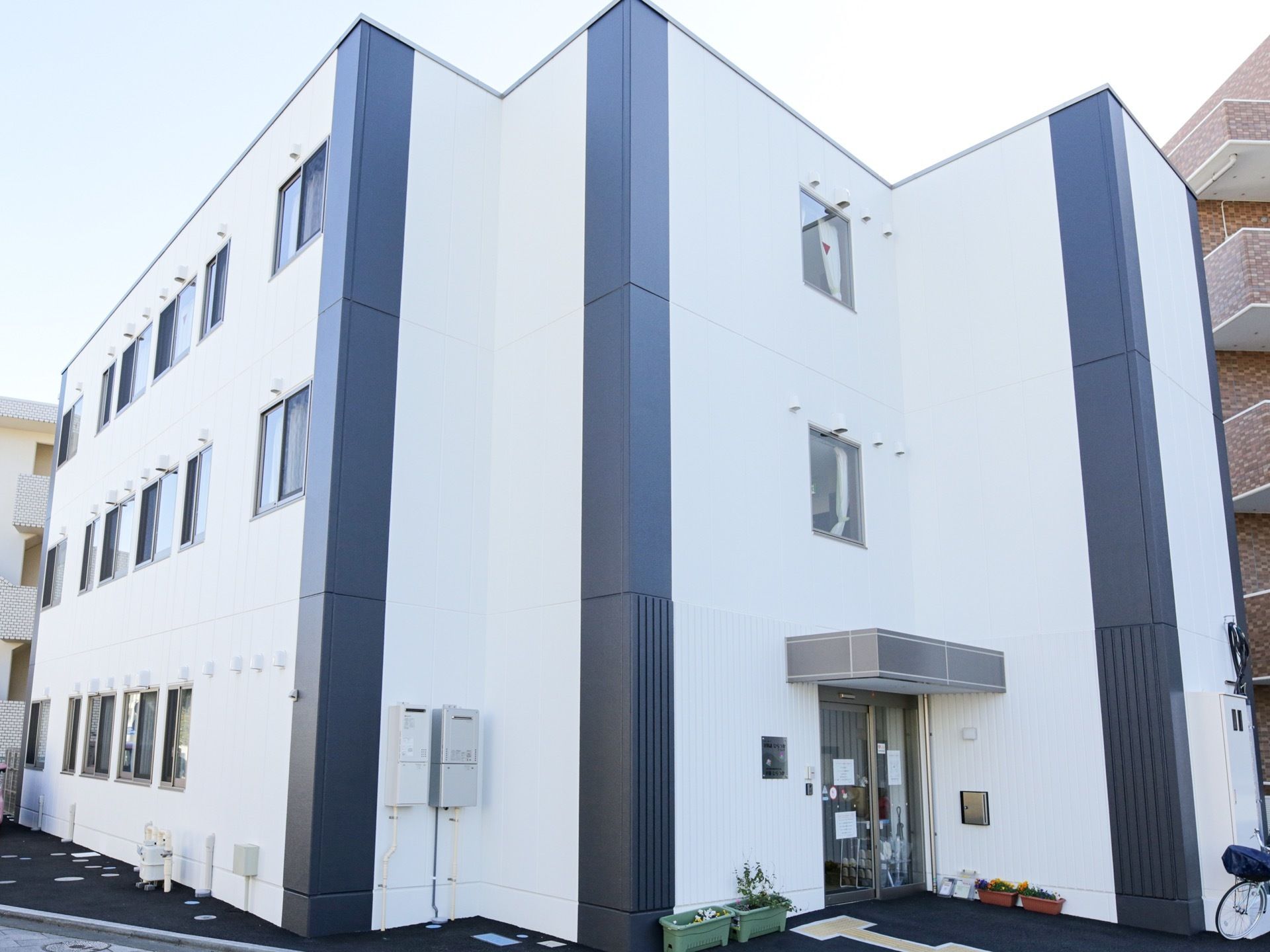 白色と濃い灰色のツートンカラーの外壁を持つ３階建ての施設である。玄関の扉の前まで黄色の点字ブロックが敷かれている。