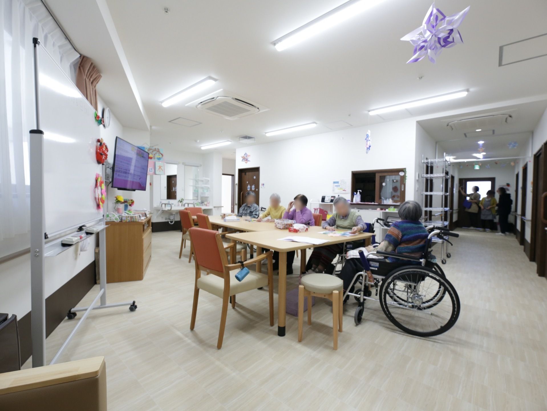 廊下のつきあたりが食堂になっている。入居者様が５名、テーブルの周りに集まっている。車椅子のままでテーブルにつくことができる。