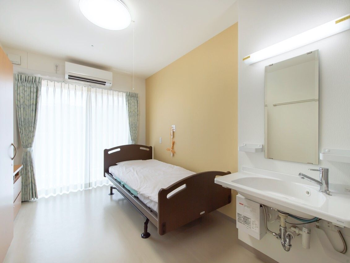車いす対応の洗面所もある一人部屋には寝具付きのベッドが置かれ、エアコンも付いている。