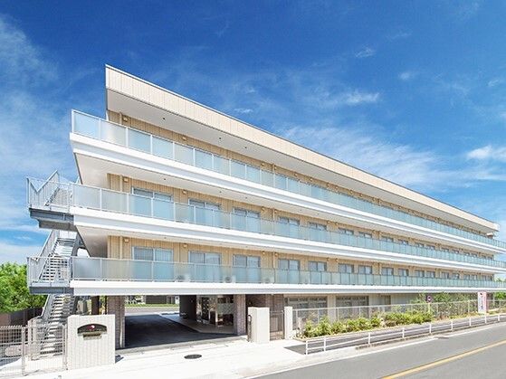 4階建ての建物はベージュ系の外壁で敷地内には駐車場があり、日当たりのいい場所に建っている。