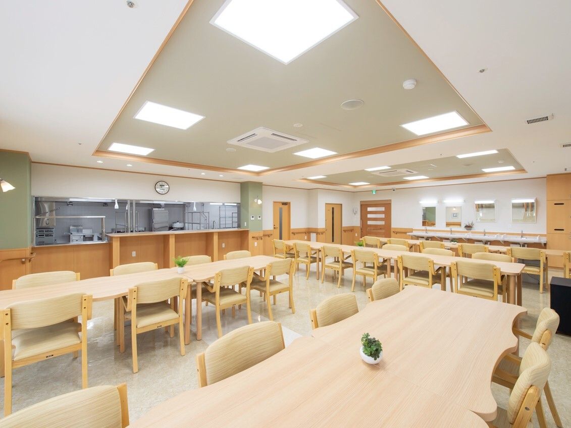 厨房がすぐそばにある食堂にはベージュの椅子がセットされた木製のダイニングテーブルセットが複数置かれている。