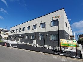 2階建ての建物はフロアにより外壁の色が異なり、白とダークグレー。広い駐車場もある。