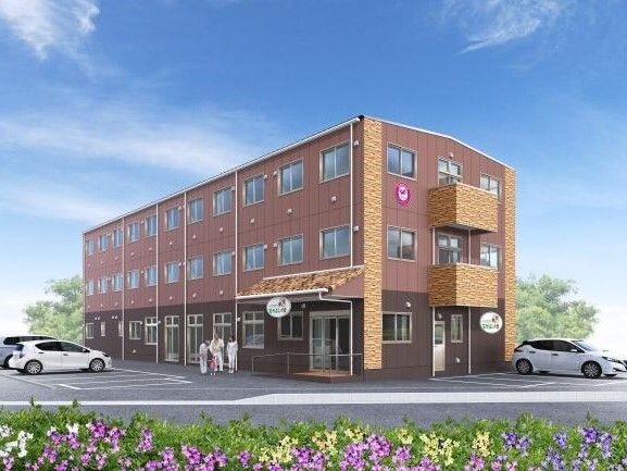 3階建ての建物。ブラウン系で明るい雰囲気。敷地内には駐車場があり、車が止まっている。数名の人が玄関のそばにいる。