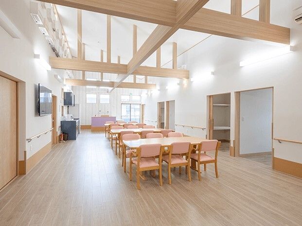 広々とした食堂は天井が高く、天窓から陽の光が差し込んでいる。ピンクの椅子がセットされたダイニングテーブルが複数ある。