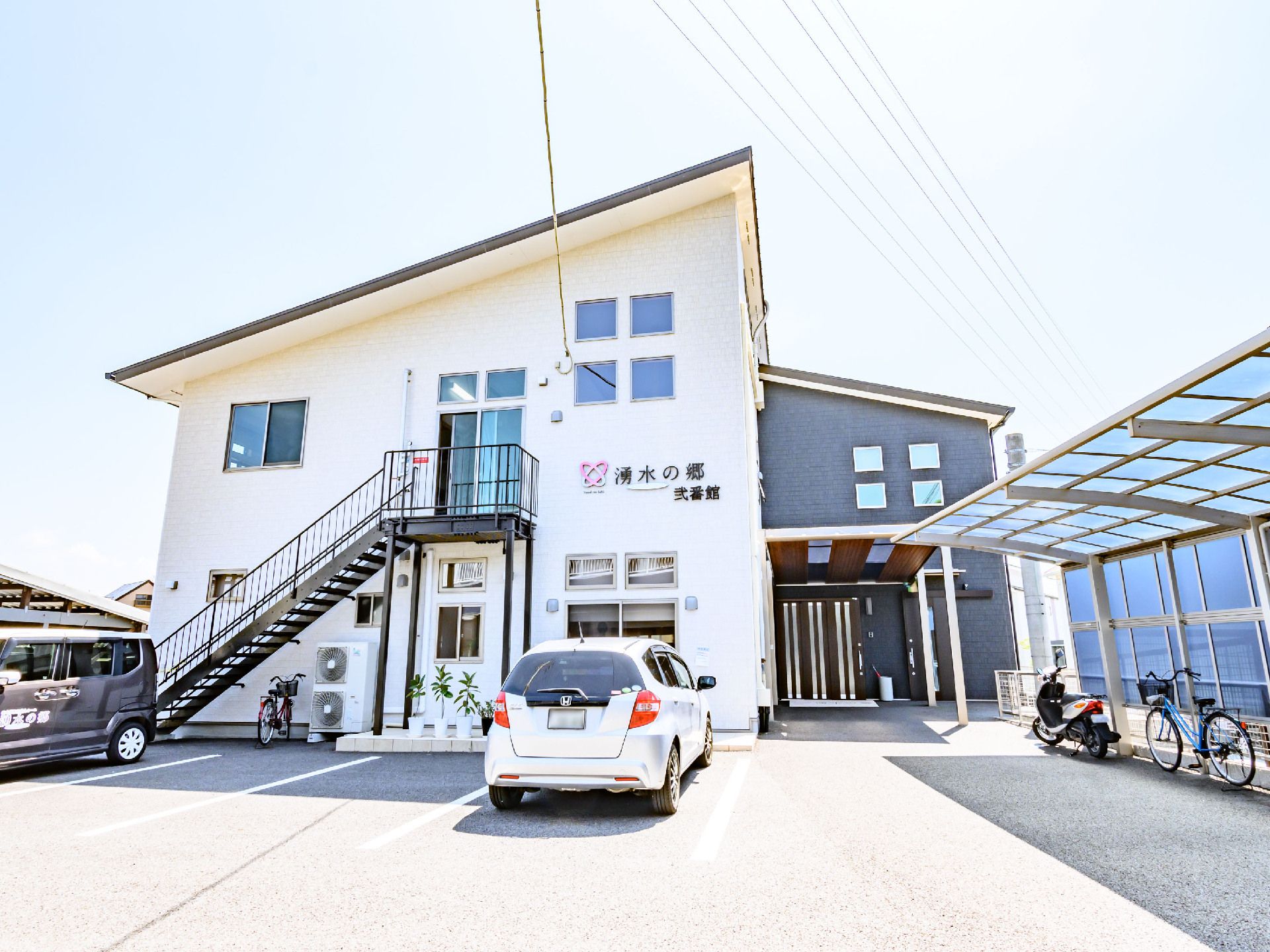 目の前に白い車が止まっている白い外観で２階建ての建物