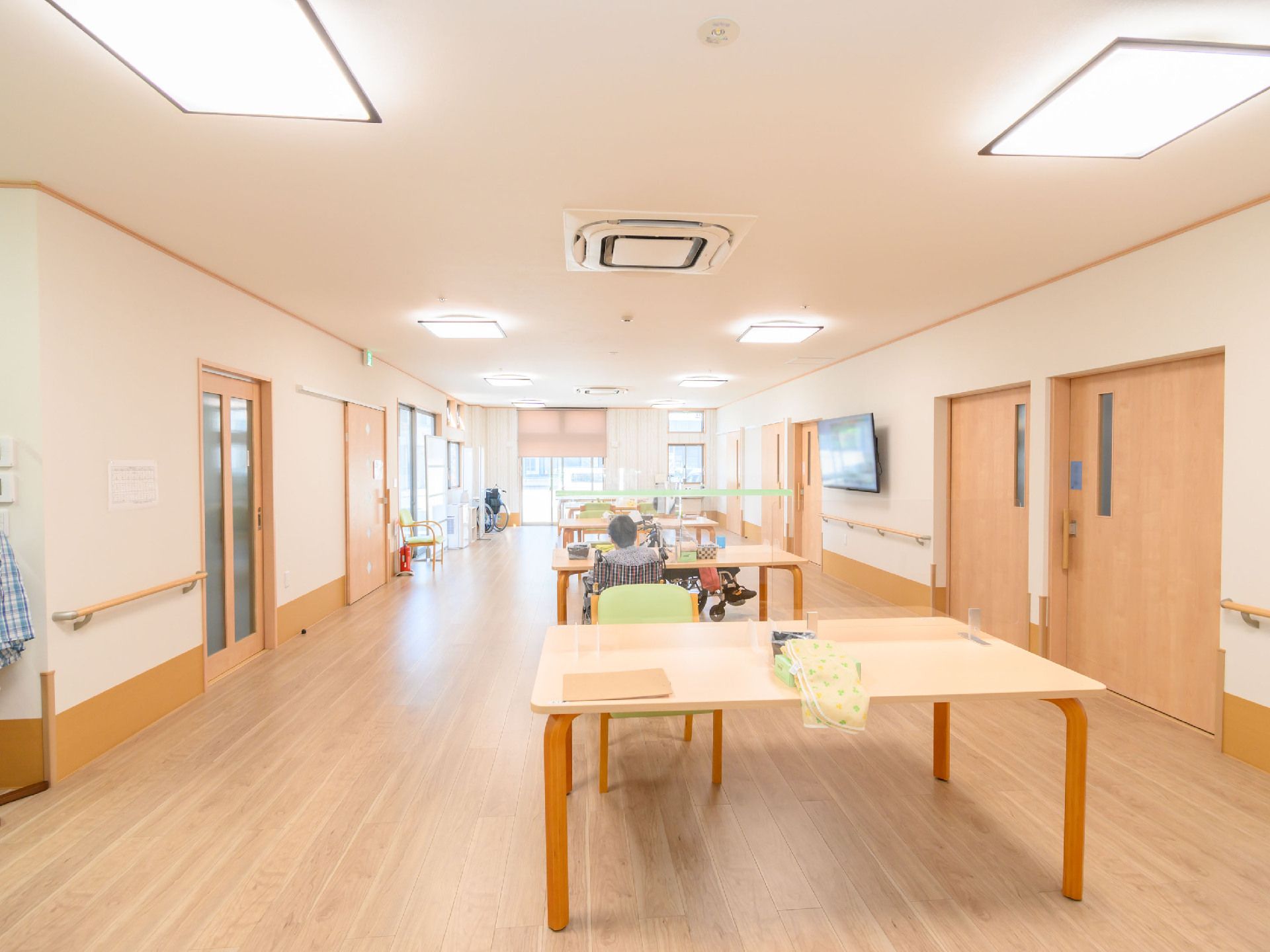 木製の扉が並んだ白い壁の広間に置かれた木製の机と椅子