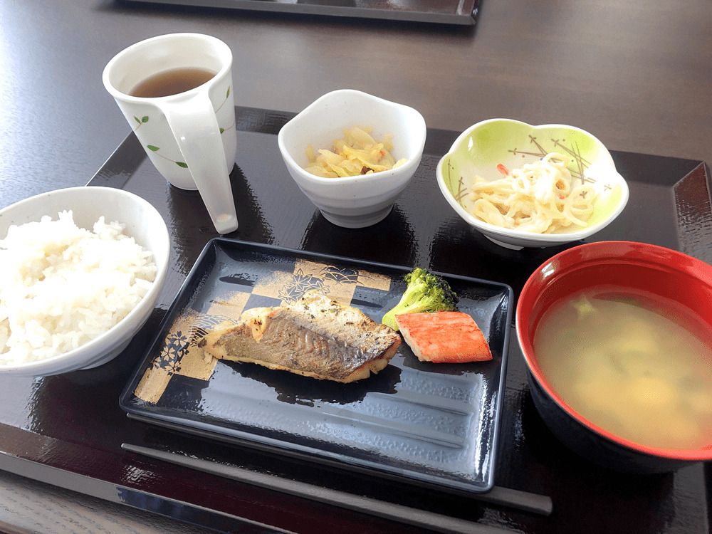 焼き魚がメインで、白いご飯やみそ汁、野菜の小鉢などが並んだトレーにはお茶もある。