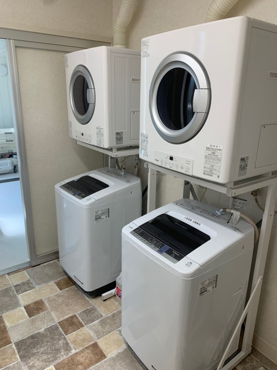 縦型の洗濯機の上には乾燥機が付いたペアが二組あり、フロアはモザイク模様。