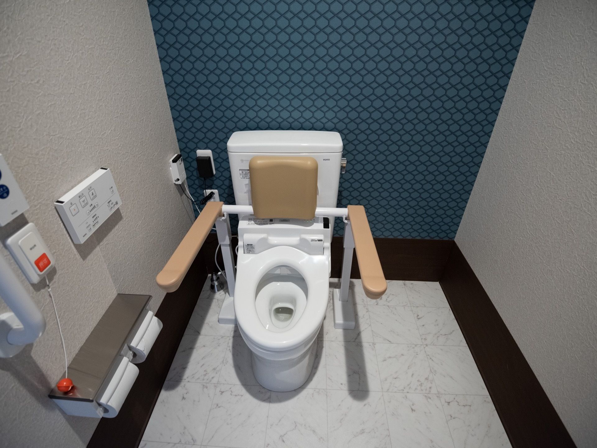 落ち着いた雰囲気のトイレである。温水洗浄便座が採用されており、快適に利用することができ、操作ボタンは壁に取り付けられている。