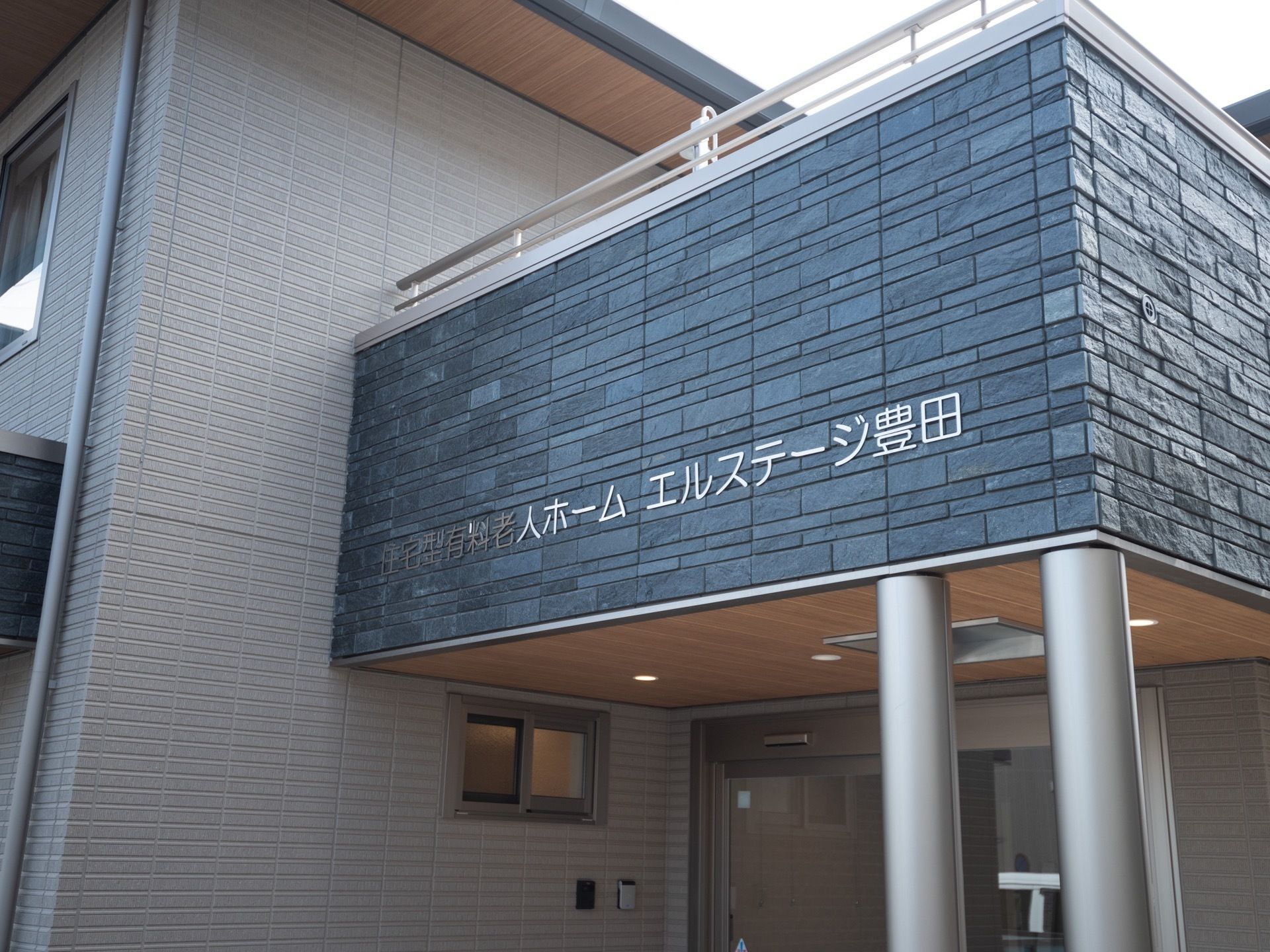 玄関前のスペースに屋根が設置されている。施設名が書かれており、雨に濡れずに施設内に出入りすることができる。