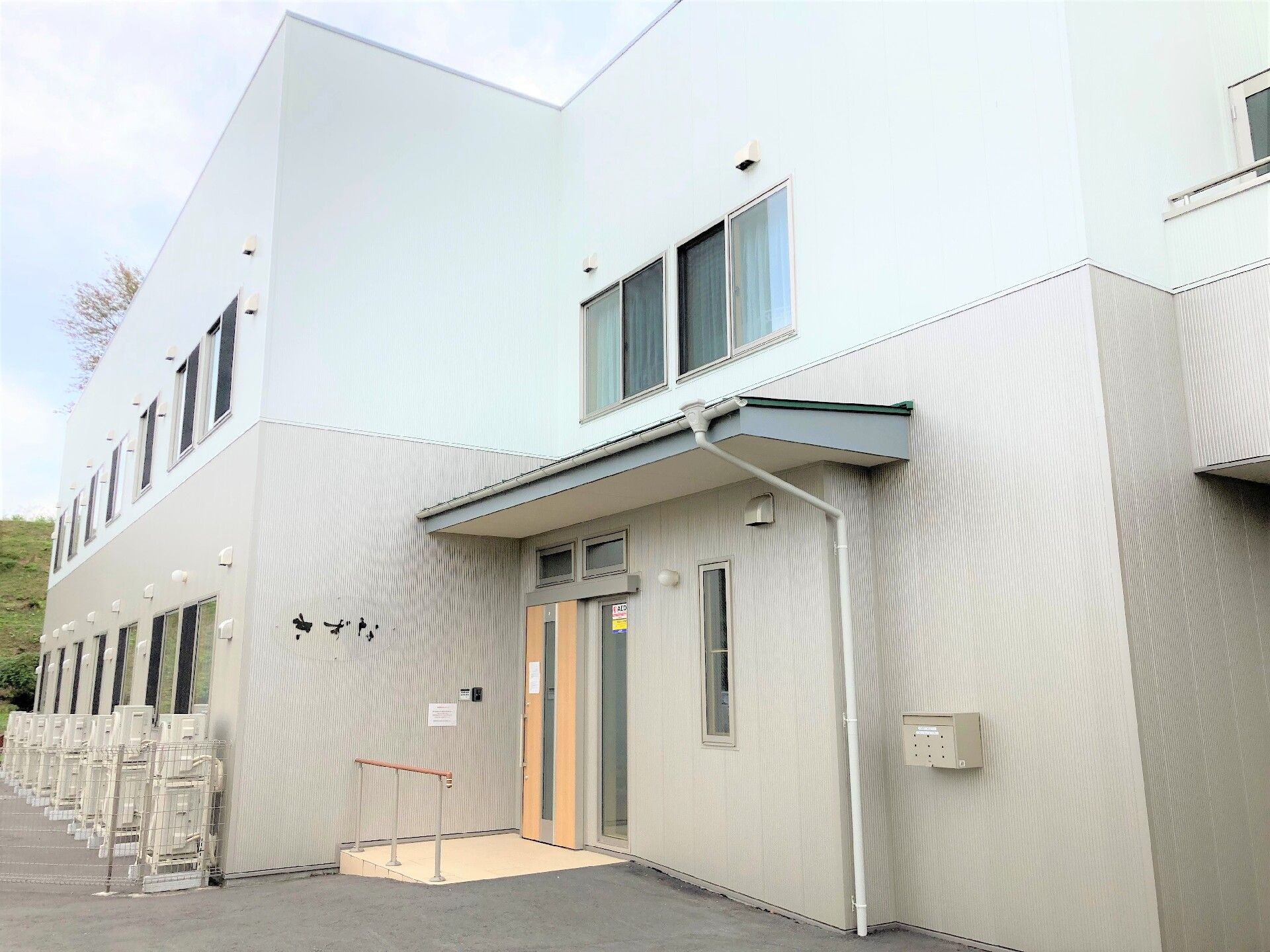 パジャマ姿でベッドに横になっている高齢女性に温かく介護に当たるエプロン姿の女性スタッフ。