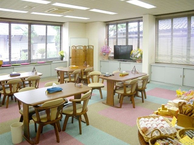 長机に椅子がたくさん並んでいる施設内の共有スペース。明るい部屋の様子が写っている