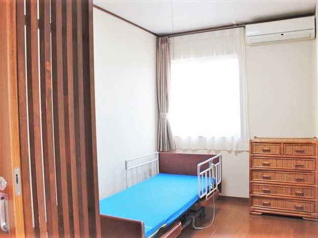 たんすと介護用ベッドが置いてある施設内の個室。エアコンが置いてある小さな部屋
