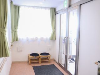 右側に出入り口がある施設のエントランス。腰かけようの椅子が置いてあるのがわかる