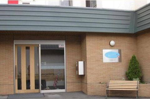施設玄関の側に造り付けられた植え込みのそばに置かれた木製ベンチ