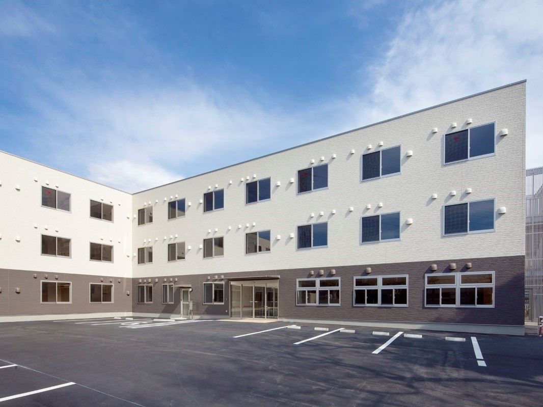 エル字型の3階建ての建物はモノトーン。玄関は自動ドアで、駐車所が広い。