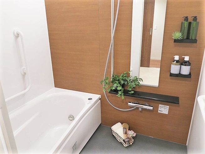茶色い壁と白い壁の浴室。細長い鏡の前には、観葉植物が置かれている。