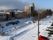 雪が降った道路。手間には数台の車が止まっていて、周辺には住宅や街路樹が見える。