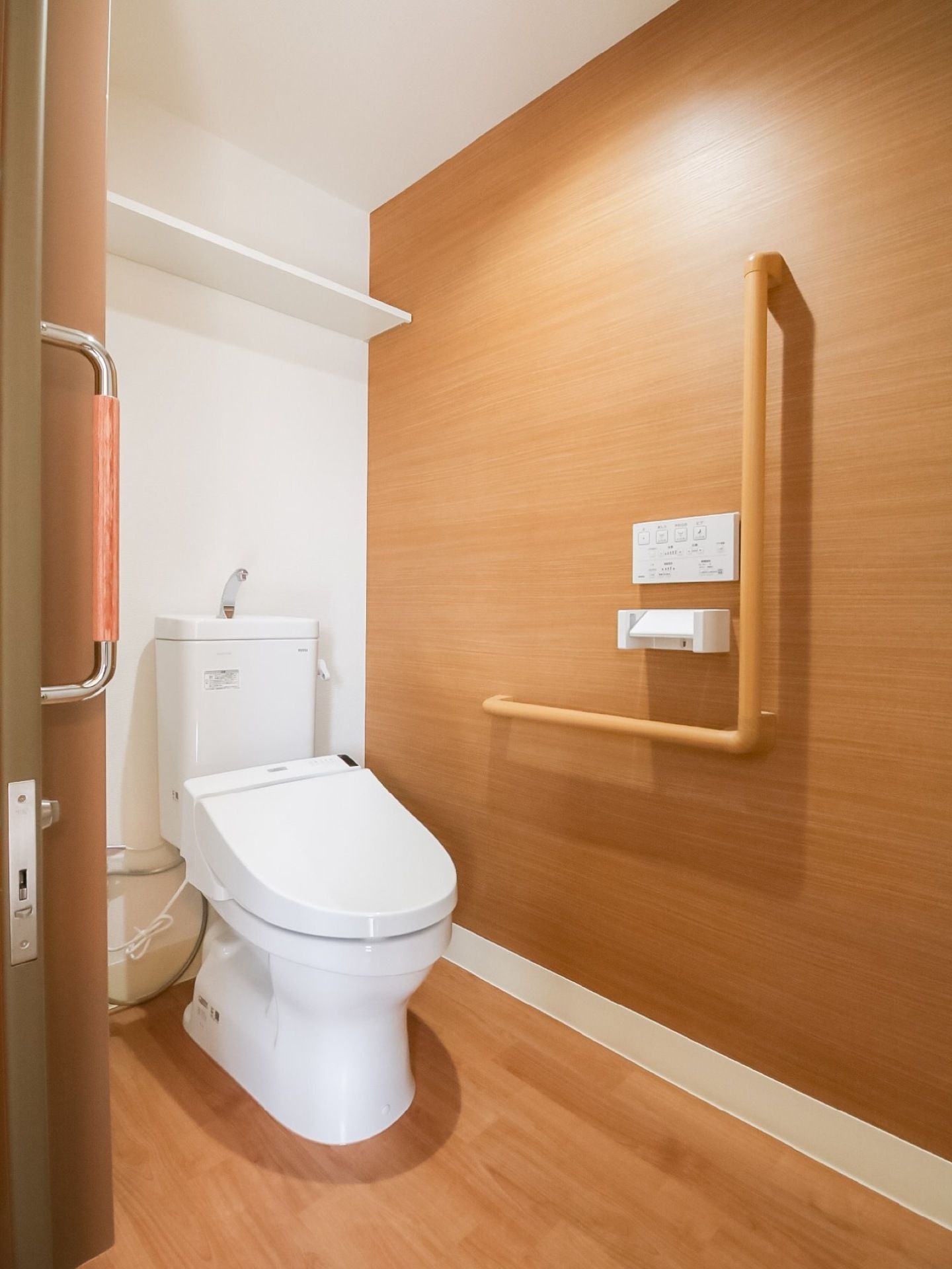 木目調の床と壁が落ち着きを感じさせるトイレである。要所に手すりが完備されているので安全に利用ができる。