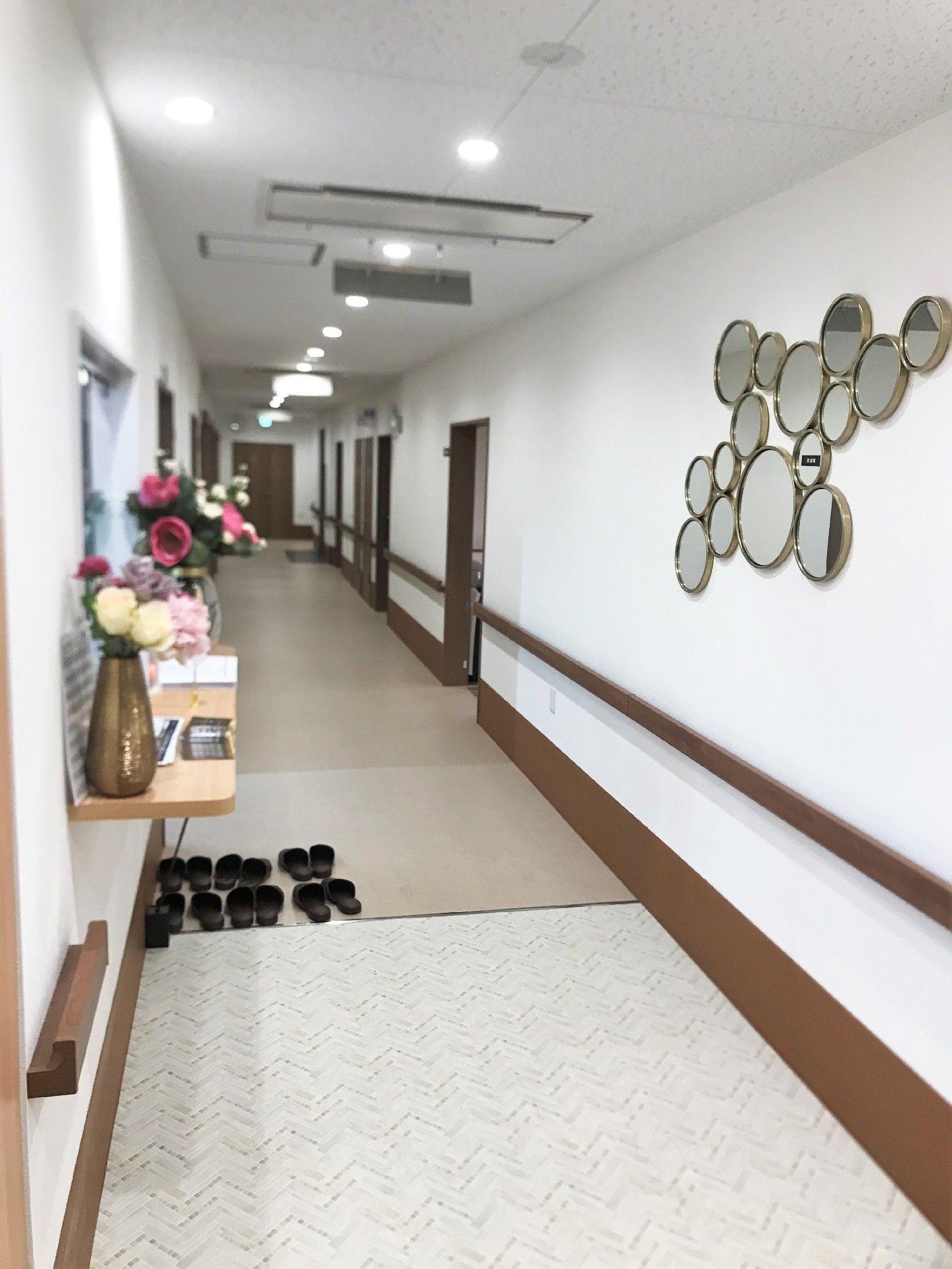 まっすぐな廊下の両サイドに手すりと居室ドアがあり、手前には花が飾られた受付スペースがある。