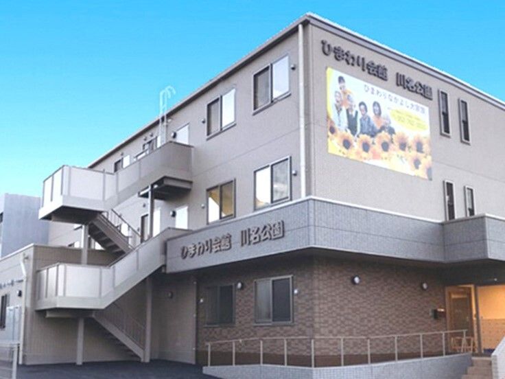 3階建ての建物の玄関には手すり付きのスロープがあり、屋外階段も付いている。外壁にはホーム名が書かれた看板がある。