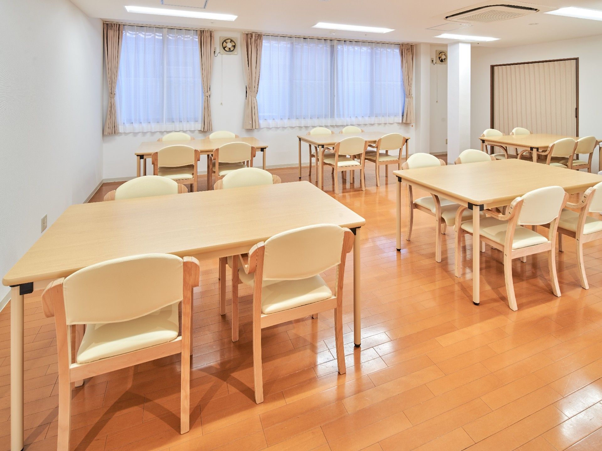 四人掛けのテーブルと椅子が複数組並んでいる施設内のリビングの様子