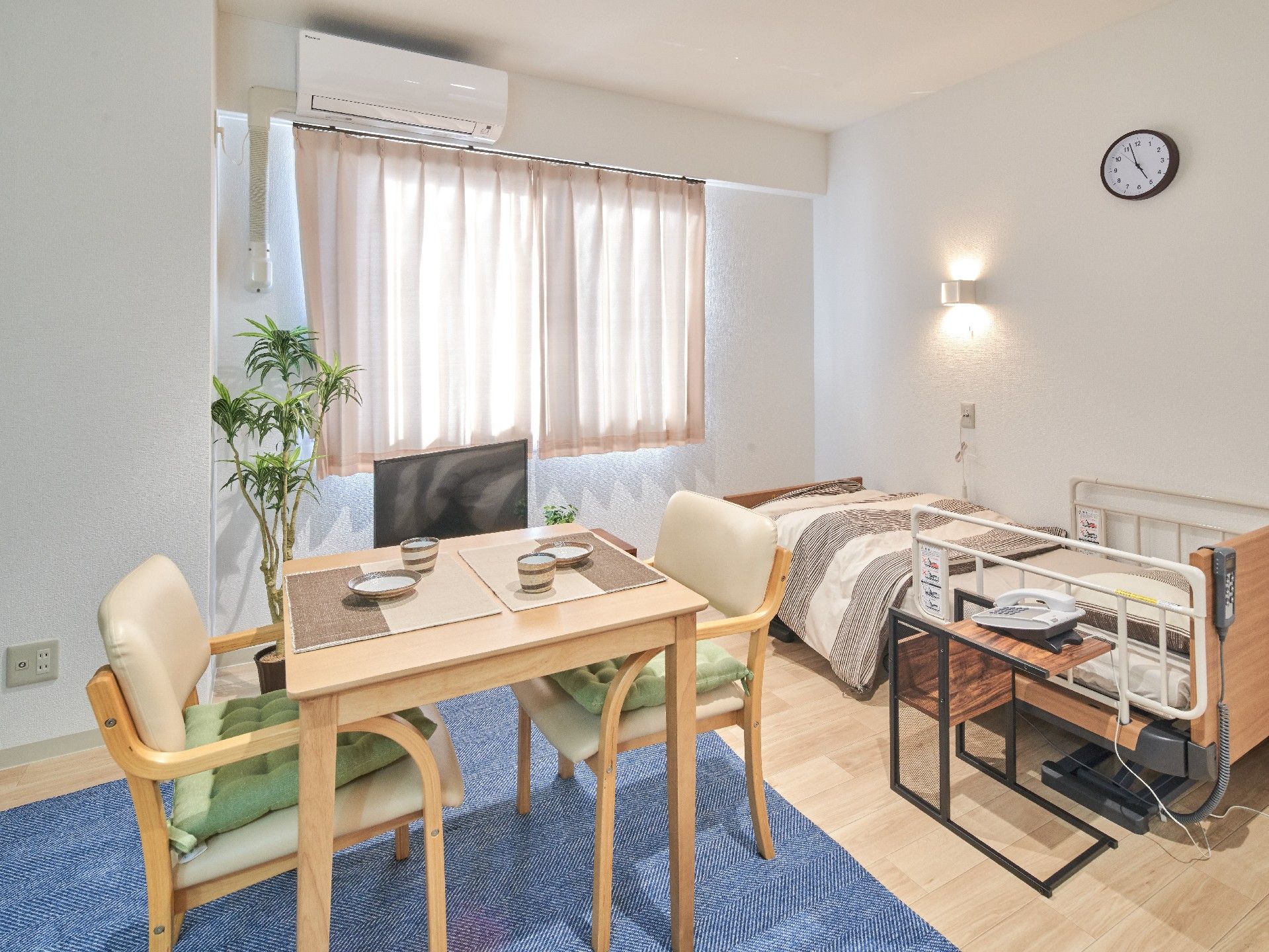 エアコンとテレビ、小さなテーブルやいす、ベッドが整ったワンルームタイプの部屋