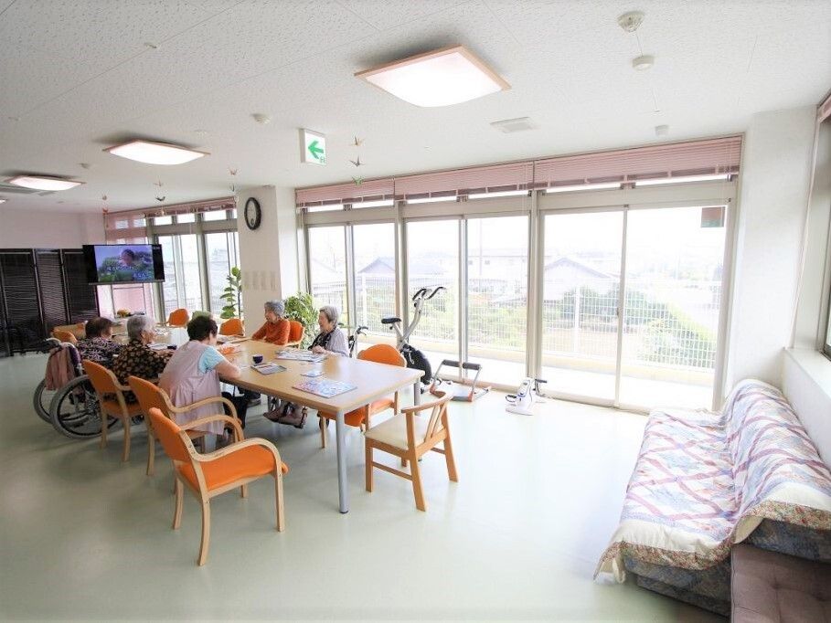 大きな窓の外には緑が広がり、ゆったりとした雰囲気。大きな長方形のテーブルには複数名の入居者がいて、車いすの利用者もいる。