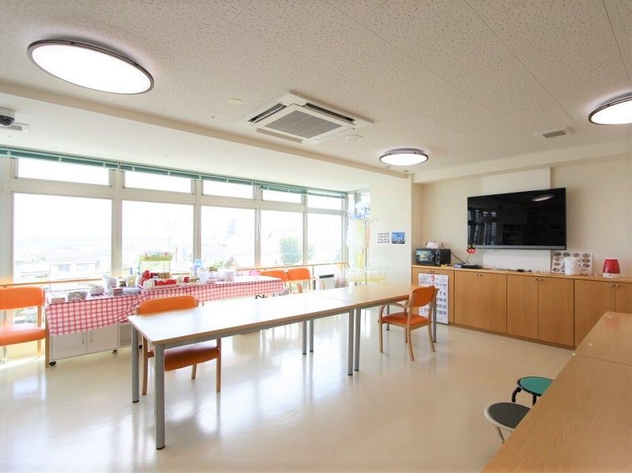 大きな壁掛けテレビが設置された食堂には車いすの人のためのスペースが開けられた長方形のダイニングテーブルがあり、大きな窓も付いている。