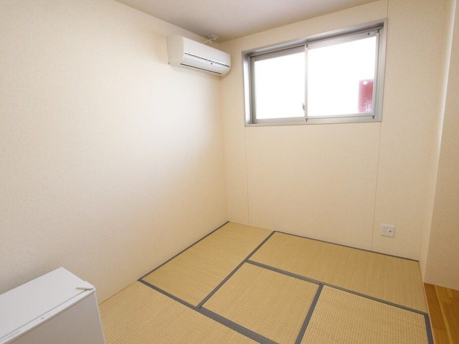 コンパクトな和風の部屋には小さな床の間があり、畳が敷かれている。壁にはエアコンが付いていて、窓にはカーテンは設置されていない。