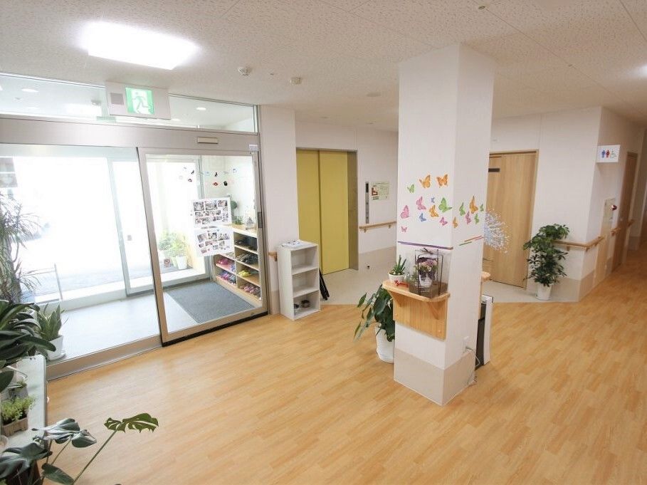 観葉植物が多く置かれた館内には手すりが設置され、玄関には自動ドアがあり、風除室も設けられている。奥にはエレベーターも見える。