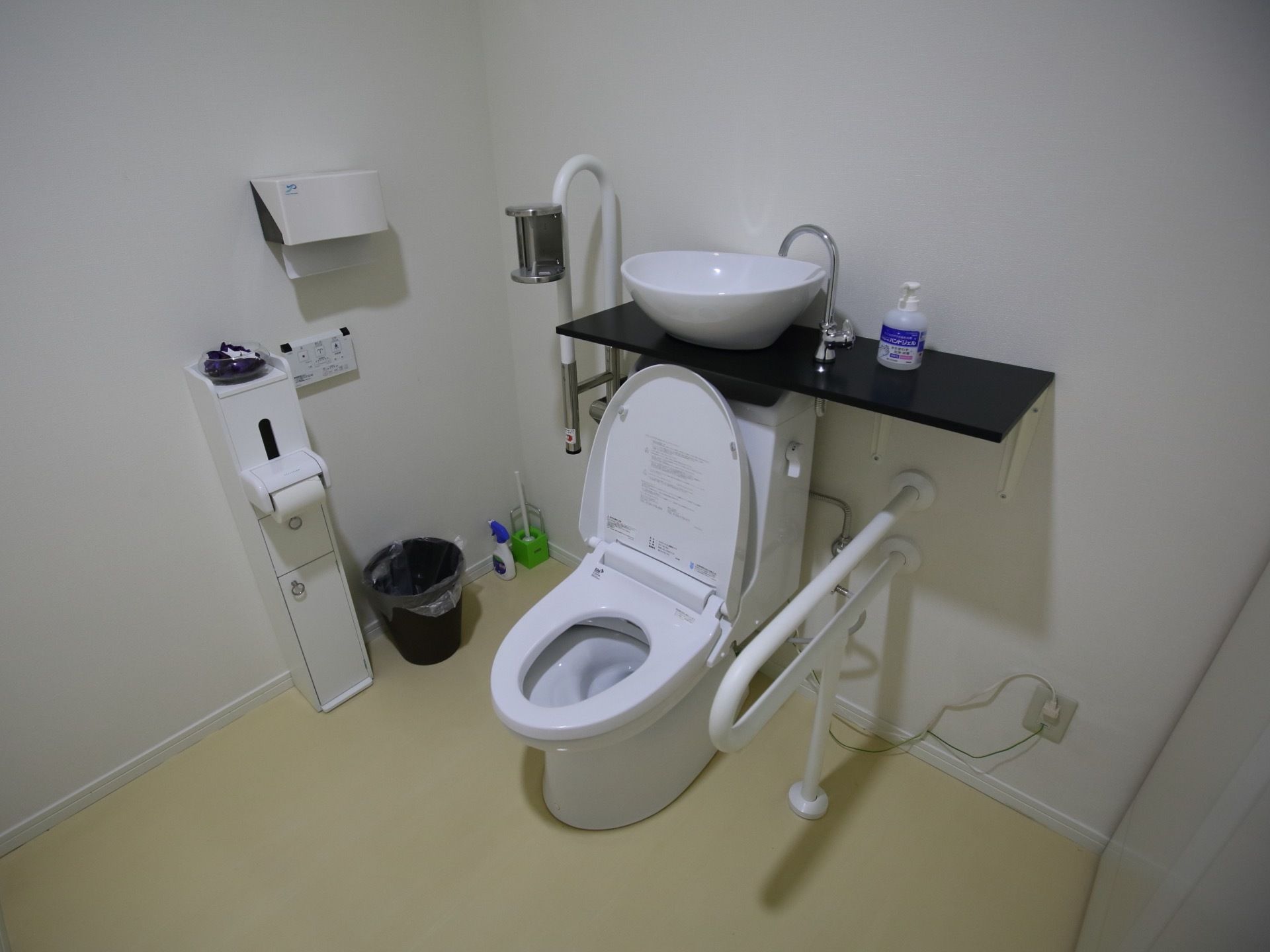 広いスペースにトイレが設置されている。ふたつき便座で、水タンクの上にある棚板の上に洗面用の鉢状のシンクが置かれている。