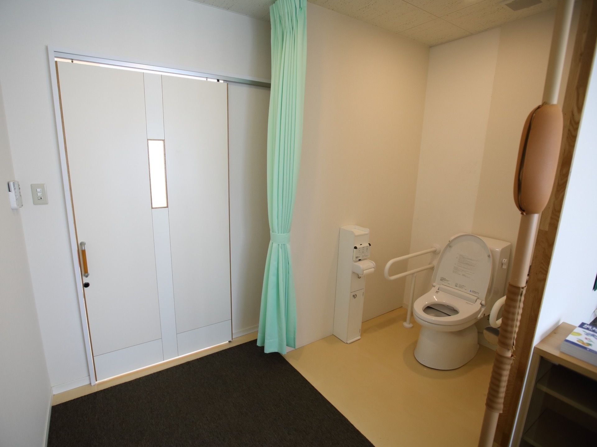 居室入口すぐの所にある広いスペースにトイレが設置されている。薄い緑色のカーテンで仕切ることができるようになっている。
