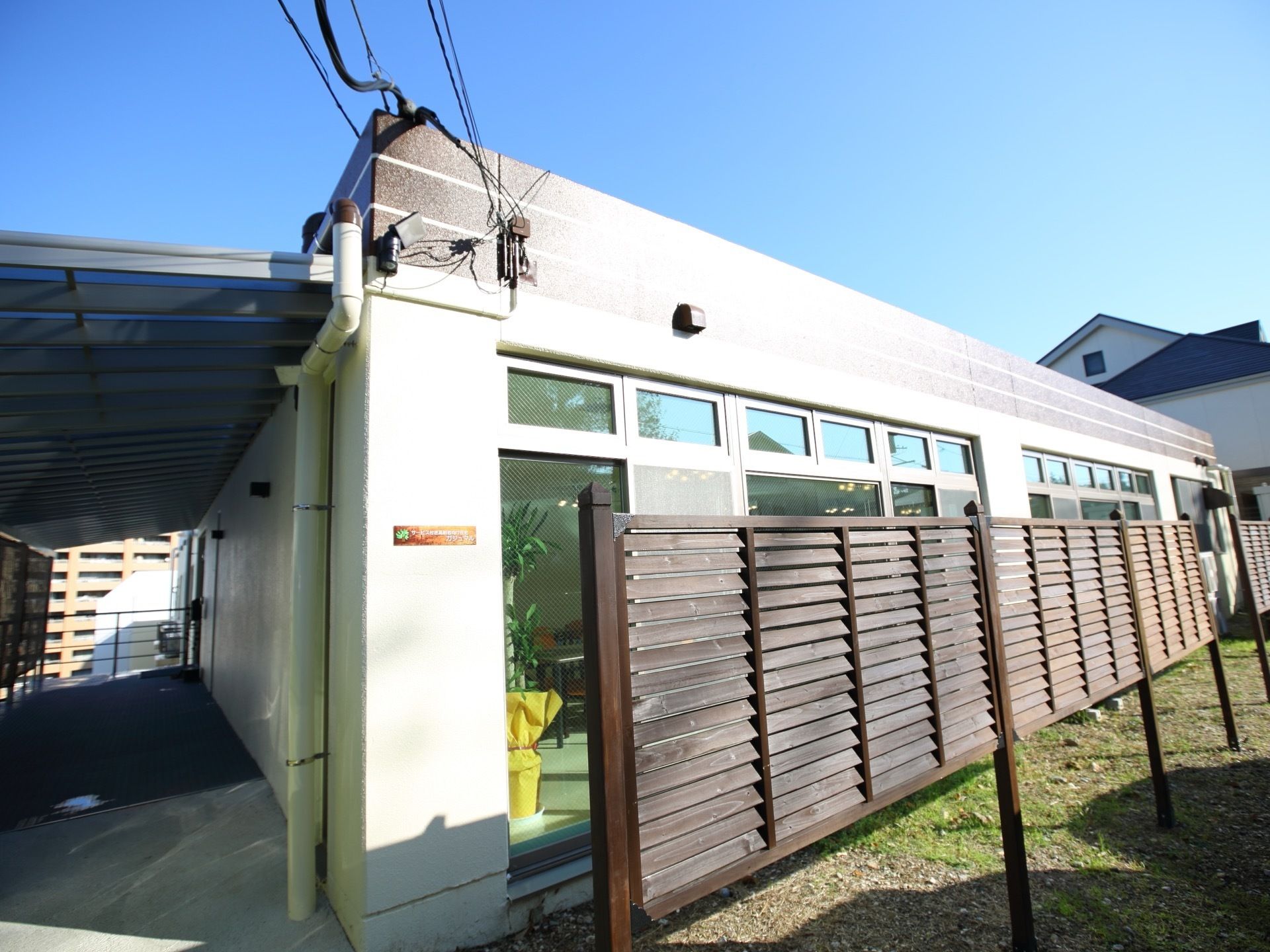 平屋建ての施設である。多く並んでいるガラス窓の前に、ルーバー上の木の板が何枚か並んで設置されている。