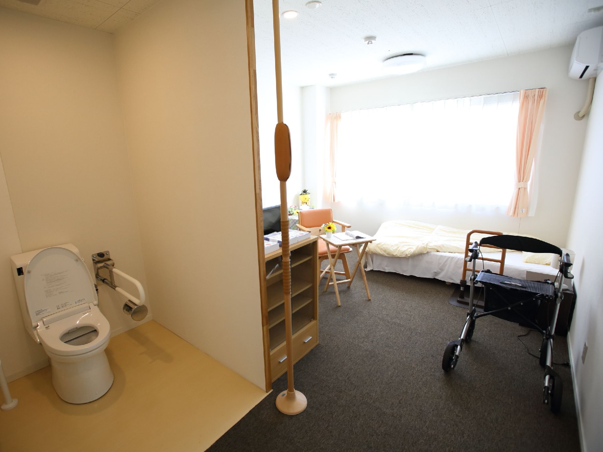 手すりが付いた広いトイレがあり、ベッドやエアコンが設置された床に段差のない居室